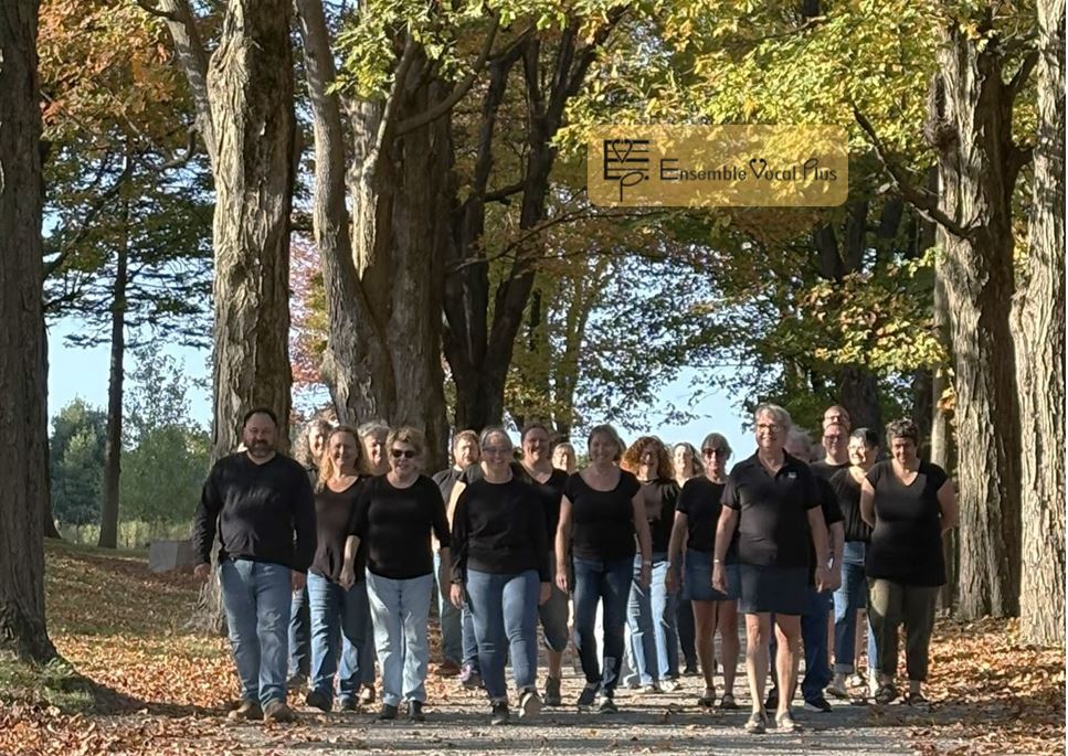 Groupe de choristes marchant ensemble sur un chemin bordé d’arbres avec le logo Ensemble Vocal Plus.