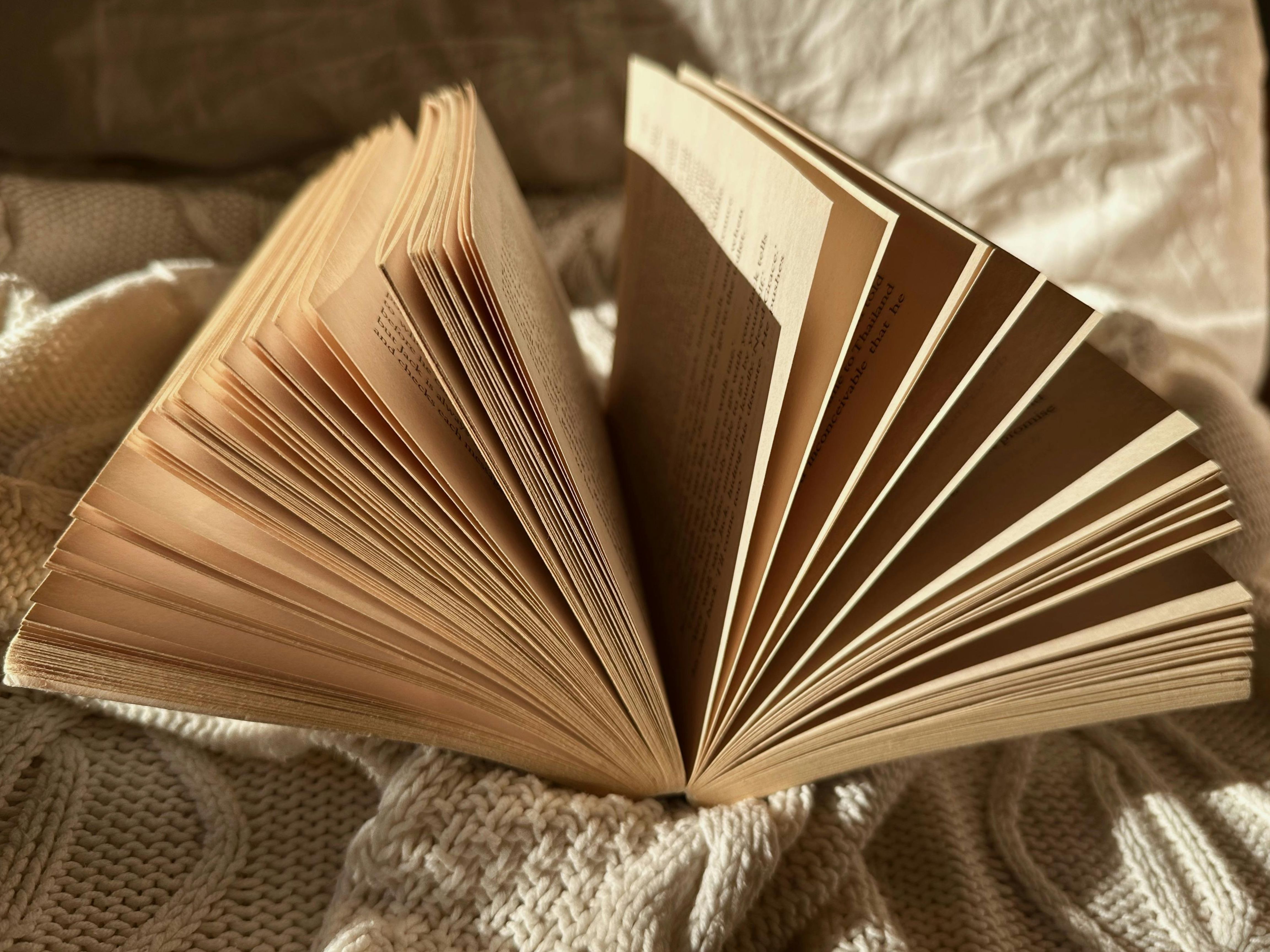reliure-japonaise-livre.jpg Livre ouvert posé sur un tissu texturé, avec ses pages déployées en éventail sous une lumière chaude, évoquant un atelier de reliure japonaise.