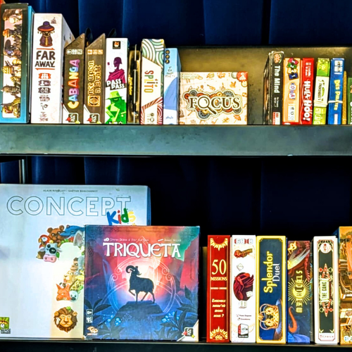 Étagères remplies de boîtes de jeux de société colorées, incluant plusieurs titres variés, illustrant une soirée de jeux de société.