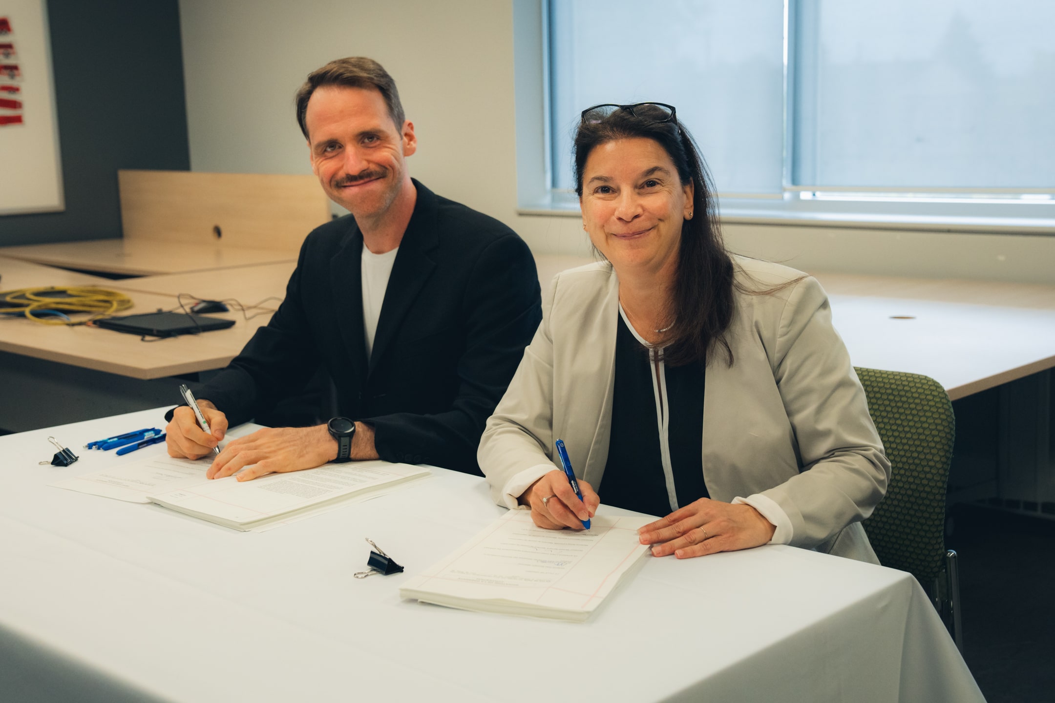 Deux personnes assises à une table signant des documents officiels.