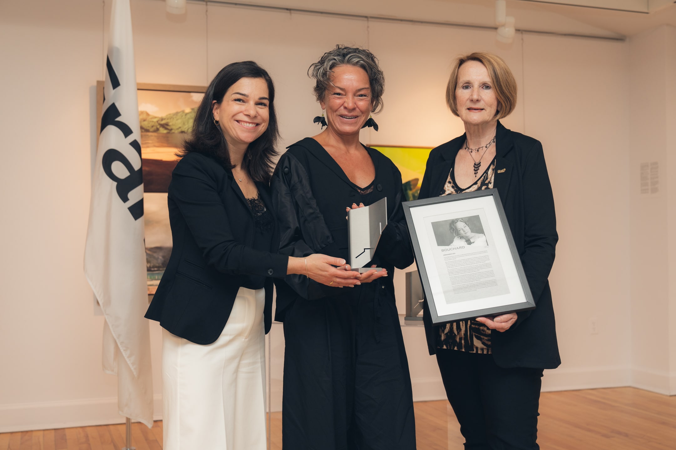 Trois personnes donc Pascale Bouchard tenant un trophée et un cadre avec texte et photo.