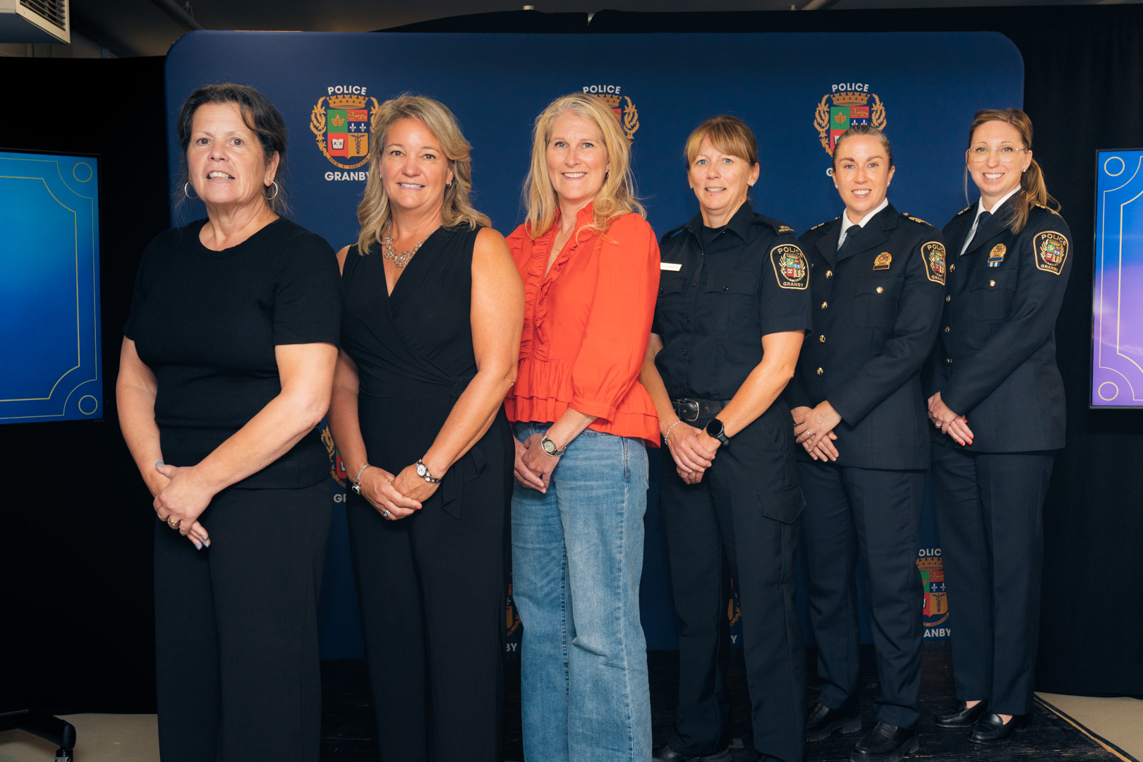 Groupe de six femmes posant devant un fond bleu avec le logo Police Granby, certaines en uniforme.